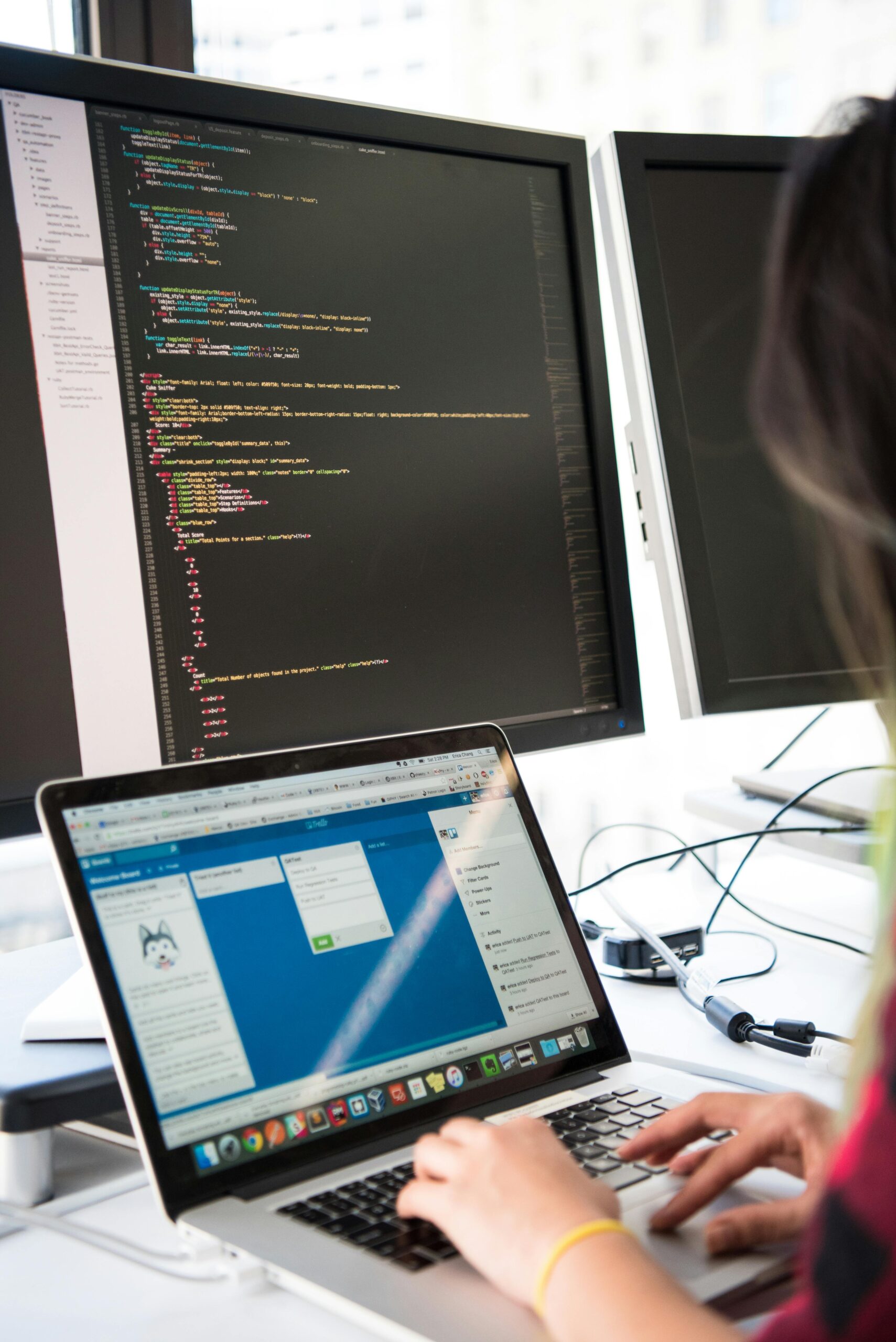 Programmer working on code across multiple screens in a modern office setting.